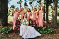 a bride and her bridesmaids pose on a bench in the woods